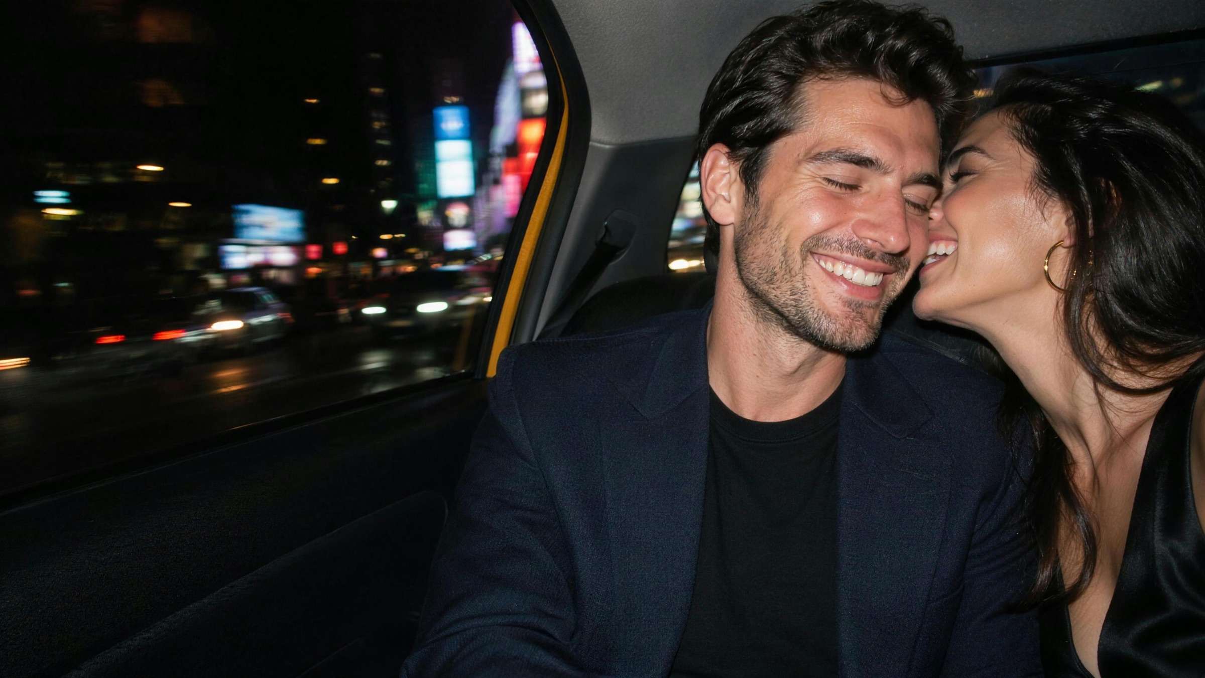 A couple laughing in the back of a New York taxi at night